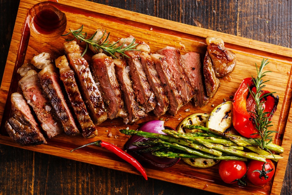 Sliced grilled Black Angus Steak Striploin and vegetables on cutting board close up